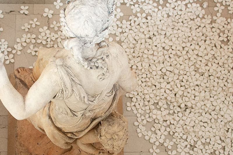 statue on gallery floor with flowers at base