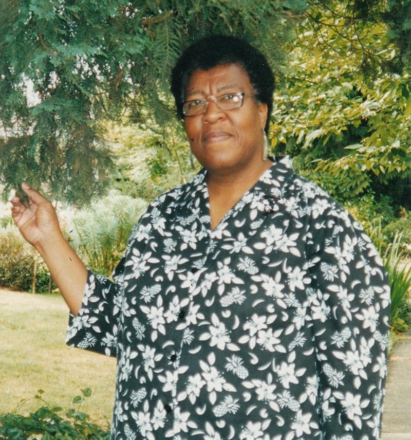 A person in a blue top with a white floral pattern grabs a branch on a tree.