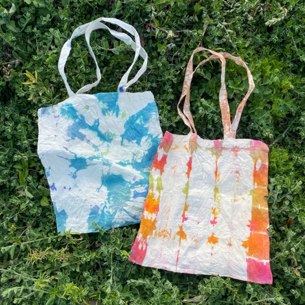 Tie-dye tote bags on a lawn.