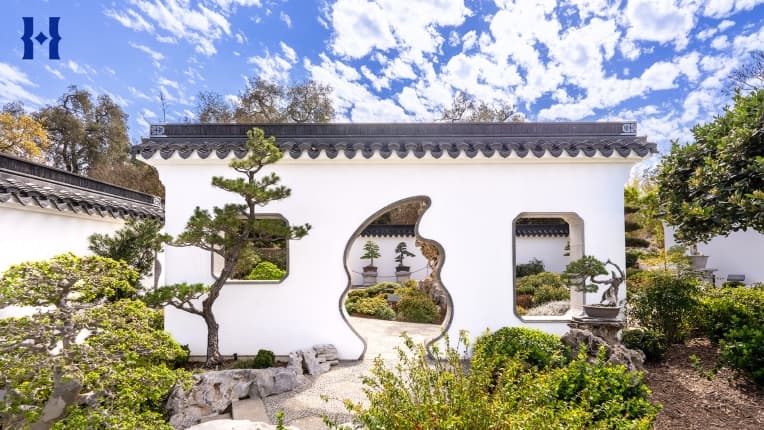 A Chinese-style garden with topiaries and a doorway through a white wall.